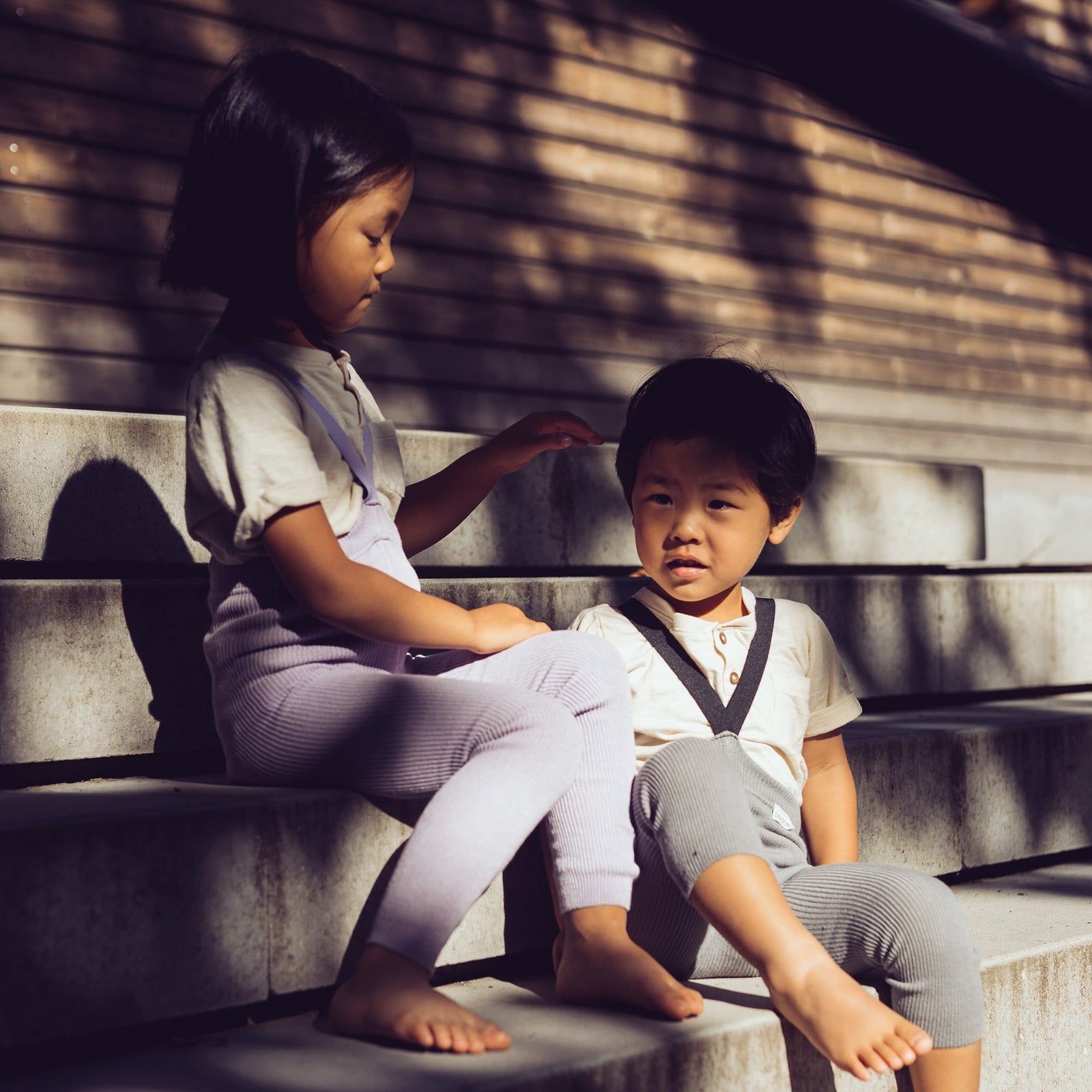 Children sitting outside on the steps, wearing Peqne products.